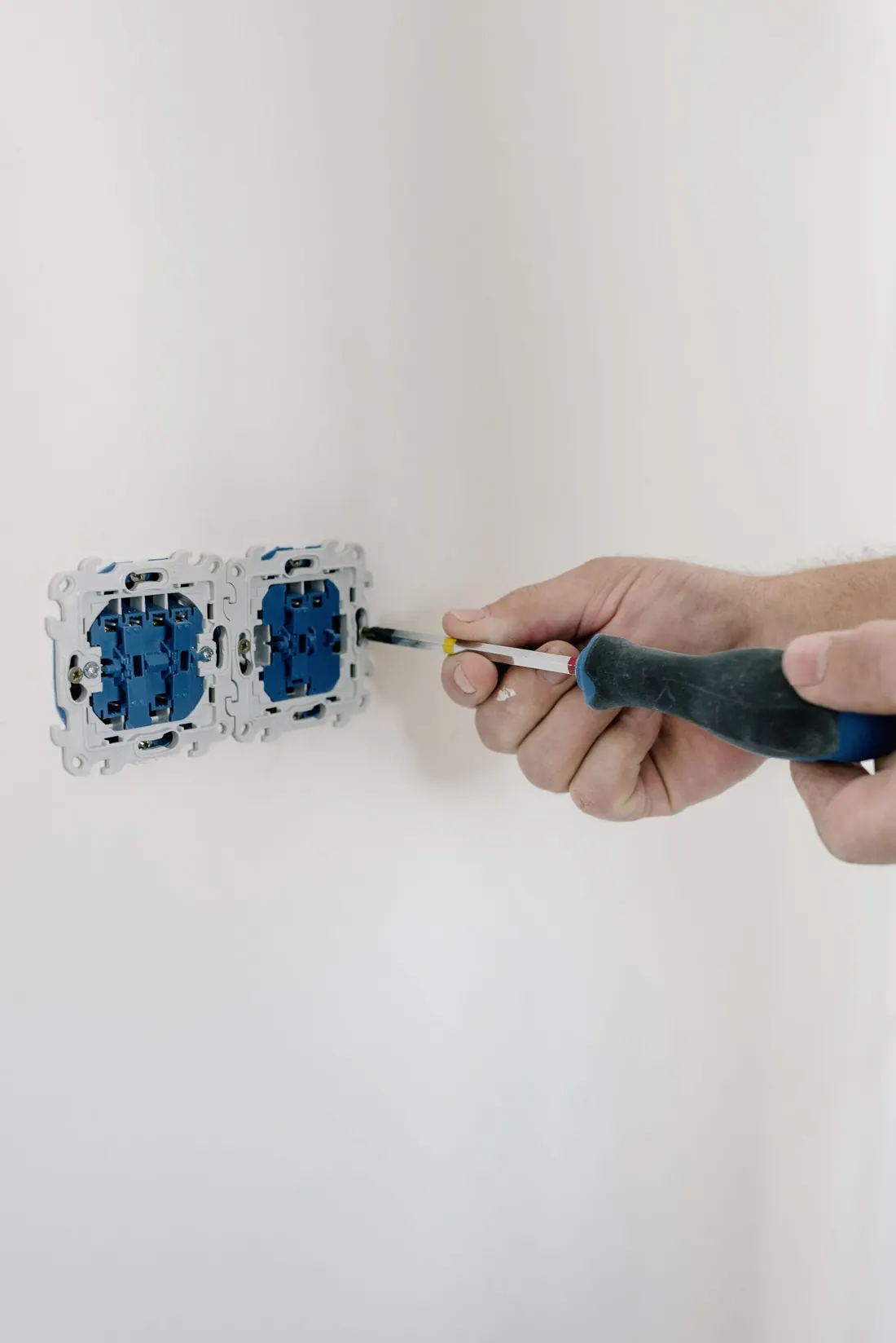 Hände setzen mit einem Schraubendreher eine Steckdose in die Wand.